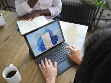 Overhead view of two people at a table working with a Microsoft laptop and notebook