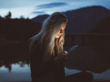 woman looking at phone beside body of water