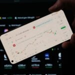 A person holding a cell phone in front of a laptop