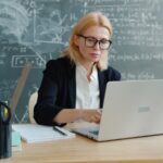 Woman working on a laptop in front of a chalkboard.