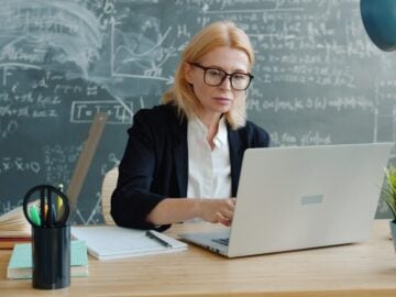 Woman working on a laptop in front of a chalkboard.