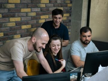 A group of people sitting around a laptop computer
