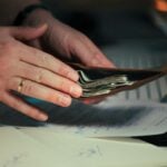Hands holding cash in a wallet over papers.