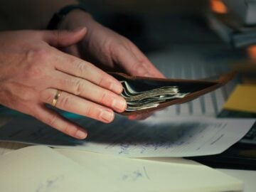 Hands holding cash in a wallet over papers.