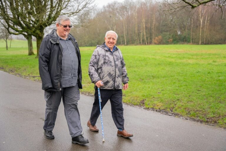 Two older men walking down a wet road
