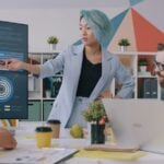 A woman with blue hair pointing at a digital chart during a team meeting