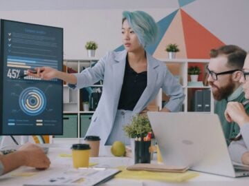 A woman with blue hair pointing at a digital chart during a team meeting